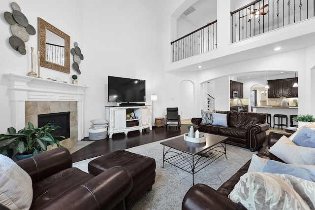 living room with hardwood / wood-style flooring, a towering ceiling, and a tile fireplace