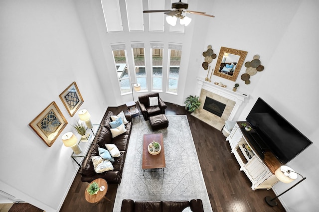 living room featuring a tiled fireplace, a towering ceiling, dark hardwood / wood-style floors, and ceiling fan