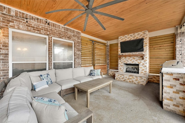 living room featuring ceiling fan, a fireplace, carpet floors, brick wall, and wooden ceiling