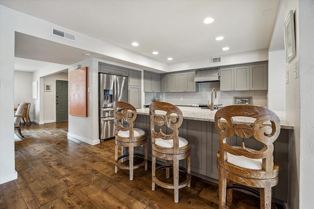 kitchen featuring a breakfast bar, gray cabinetry, dark hardwood / wood-style flooring, light stone counters, and kitchen peninsula