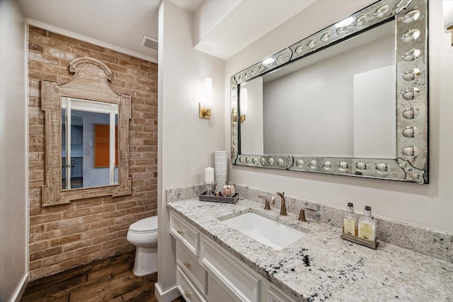 bathroom with vanity, brick wall, hardwood / wood-style floors, and toilet