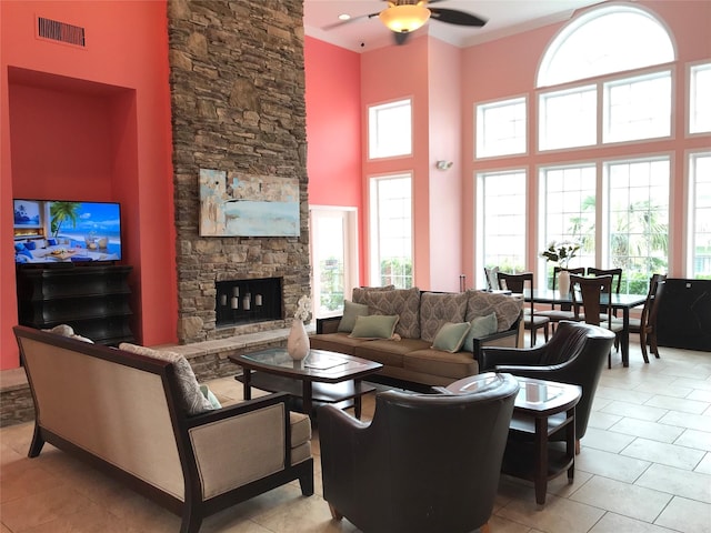 tiled living room with a stone fireplace, ceiling fan, and a high ceiling