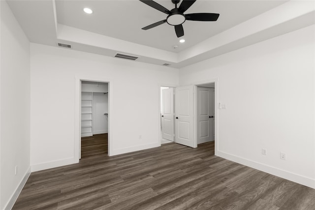 unfurnished bedroom featuring ceiling fan, a raised ceiling, dark hardwood / wood-style flooring, a walk in closet, and a closet