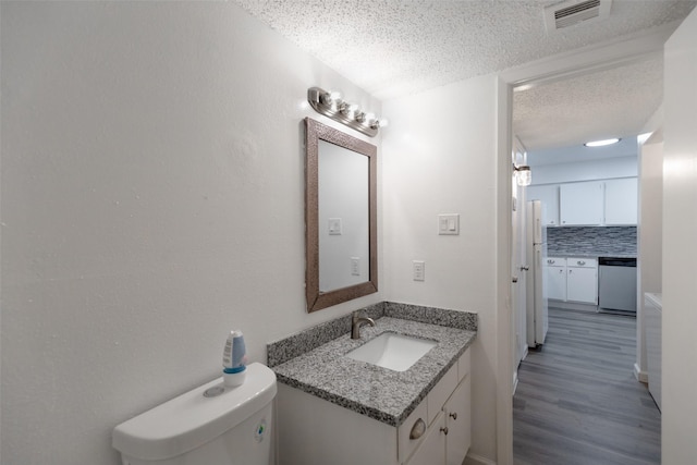 bathroom with vanity, wood-type flooring, a textured ceiling, decorative backsplash, and toilet