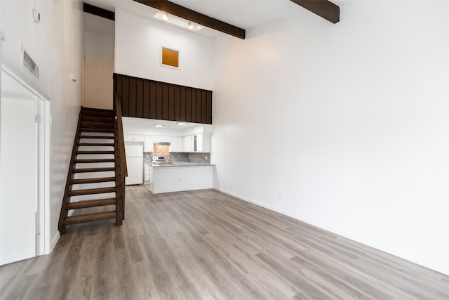 unfurnished living room featuring a towering ceiling, beam ceiling, and light hardwood / wood-style flooring