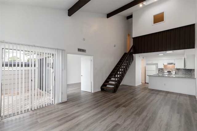 unfurnished living room with a towering ceiling, light hardwood / wood-style floors, and beamed ceiling