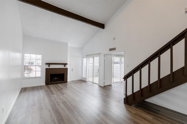 unfurnished living room featuring a brick fireplace, hardwood / wood-style flooring, high vaulted ceiling, and beamed ceiling