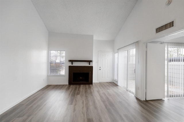 unfurnished living room featuring hardwood / wood-style flooring, a textured ceiling, a fireplace, and high vaulted ceiling