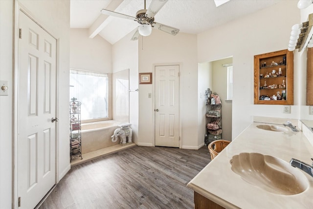 bathroom with lofted ceiling with skylight, hardwood / wood-style floors, a tub, vanity, and ceiling fan