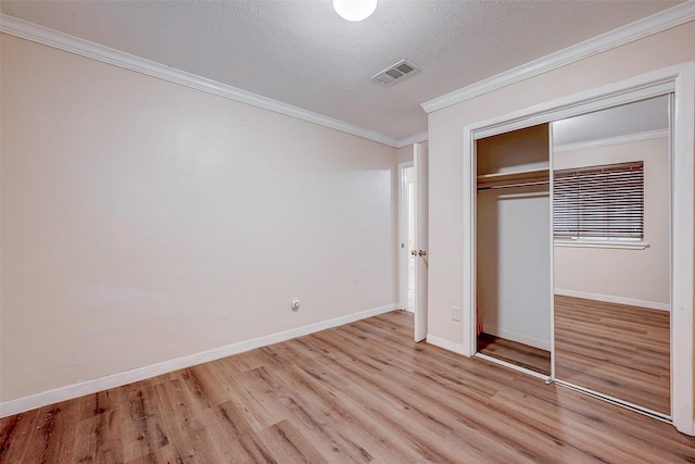 unfurnished bedroom with ornamental molding, a textured ceiling, light wood-type flooring, and a closet