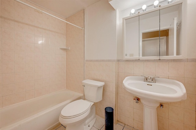 bathroom featuring tiled shower / bath, toilet, and tile walls