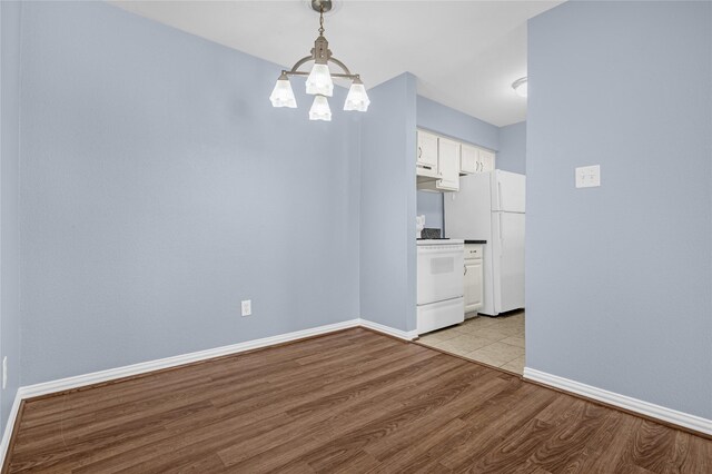 unfurnished dining area with a chandelier, light wood finished floors, and baseboards