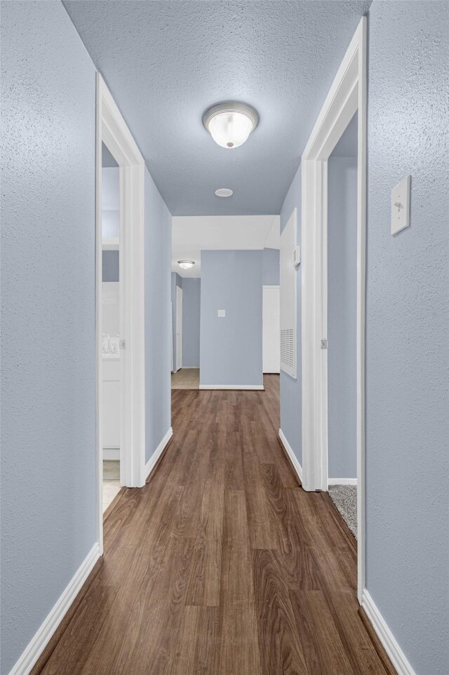 corridor with wood finished floors, baseboards, a textured ceiling, and a textured wall