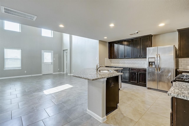 kitchen featuring a kitchen island with sink, sink, light stone counters, and stainless steel fridge