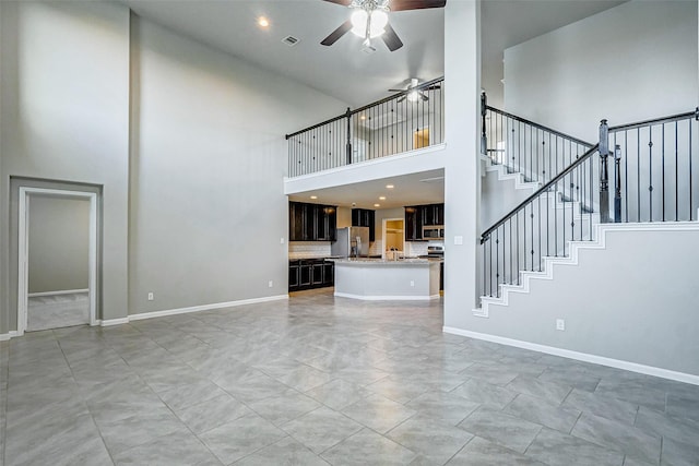 unfurnished living room with ceiling fan and a towering ceiling