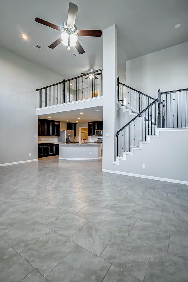 unfurnished living room with light tile patterned floors, ceiling fan, and a high ceiling