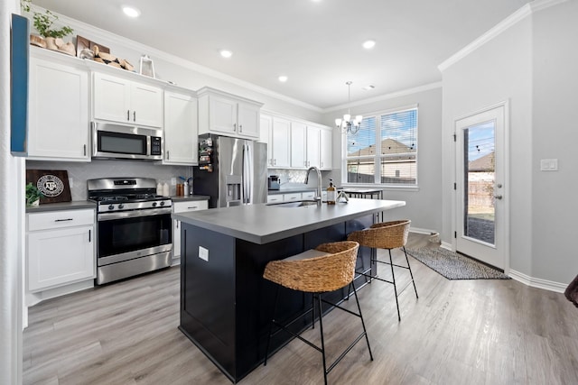 kitchen with decorative light fixtures, white cabinetry, sink, stainless steel appliances, and a center island with sink