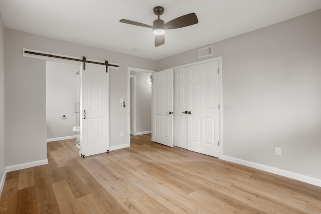 unfurnished bedroom with light wood finished floors, a barn door, visible vents, baseboards, and a closet