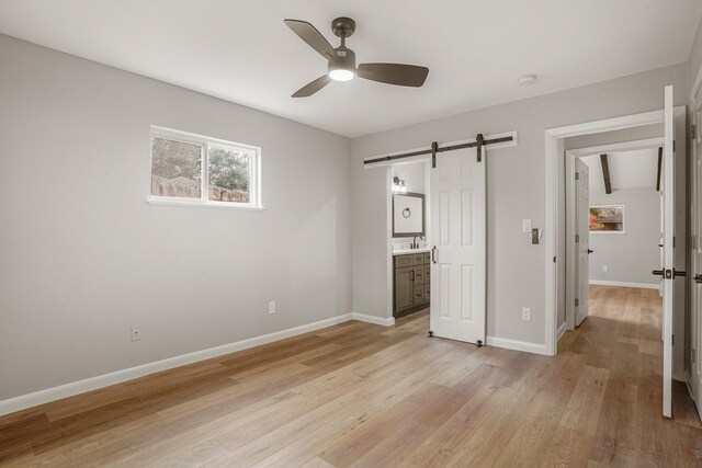 unfurnished bedroom with ensuite bathroom, sink, ceiling fan, a barn door, and light wood-type flooring