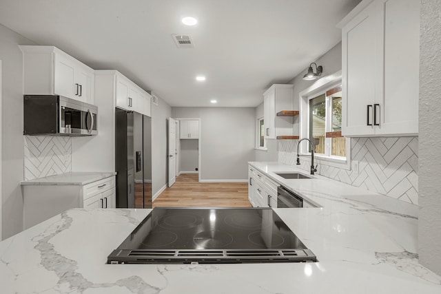 kitchen featuring light stone counters, stainless steel appliances, visible vents, white cabinetry, and a sink