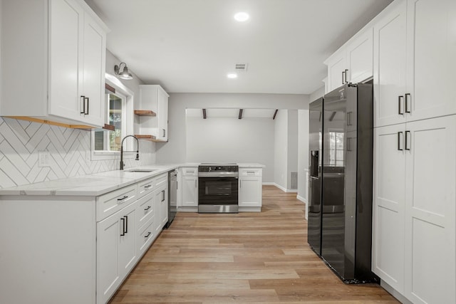 kitchen with appliances with stainless steel finishes, sink, white cabinets, and light wood-type flooring