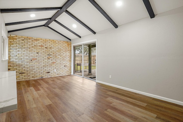 unfurnished living room featuring vaulted ceiling with beams, brick wall, and light wood-type flooring