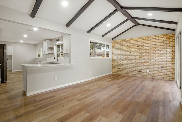 unfurnished living room featuring vaulted ceiling with beams, brick wall, visible vents, baseboards, and light wood finished floors