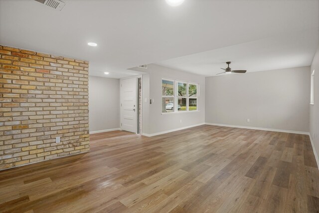 unfurnished living room with ceiling fan, brick wall, and light hardwood / wood-style floors