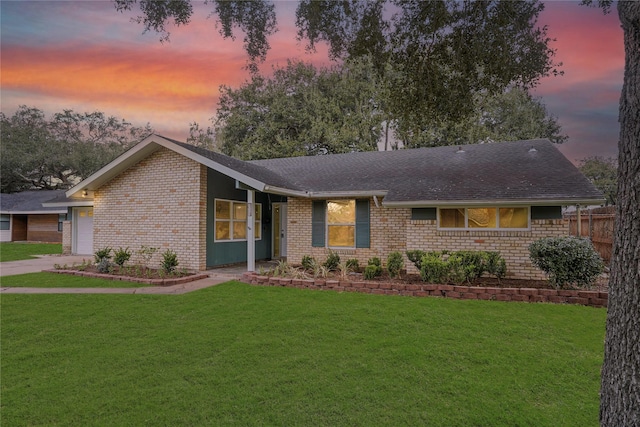 ranch-style home with brick siding, a lawn, an attached garage, and roof with shingles