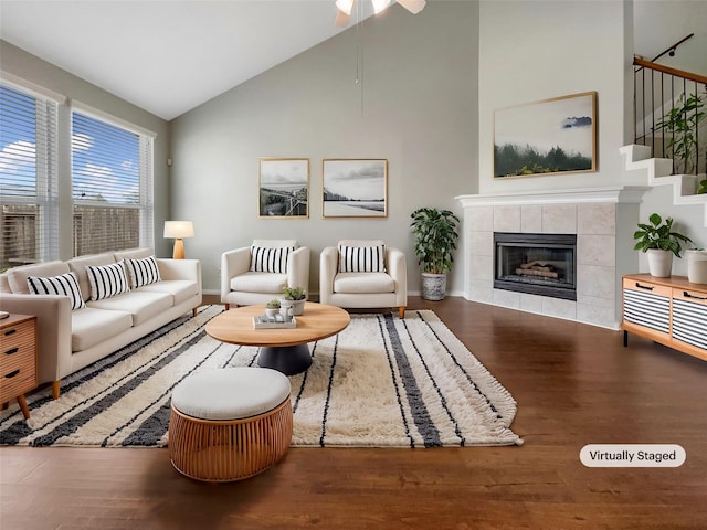 living room featuring wood-type flooring, a tiled fireplace, and high vaulted ceiling