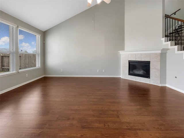 unfurnished living room featuring dark wood-type flooring, ceiling fan, a tiled fireplace, and high vaulted ceiling