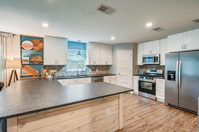 kitchen with sink, white cabinetry, light wood-type flooring, appliances with stainless steel finishes, and pendant lighting