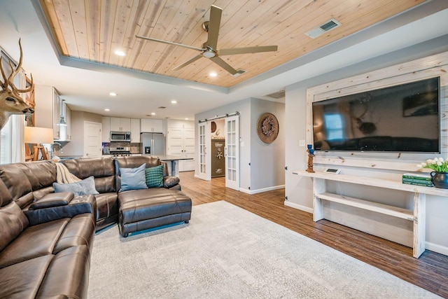 living room featuring ceiling fan, light hardwood / wood-style floors, a raised ceiling, wooden ceiling, and a barn door