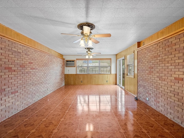 unfurnished living room featuring brick wall, wood walls, a wall mounted AC, and a ceiling fan