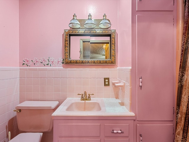 bathroom featuring toilet, a wainscoted wall, tile walls, and vanity