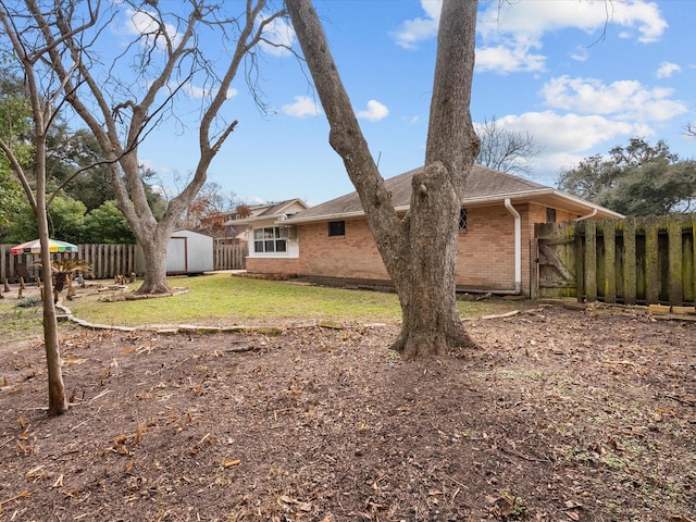 back of house featuring a storage shed, an outbuilding, fence, a yard, and brick siding