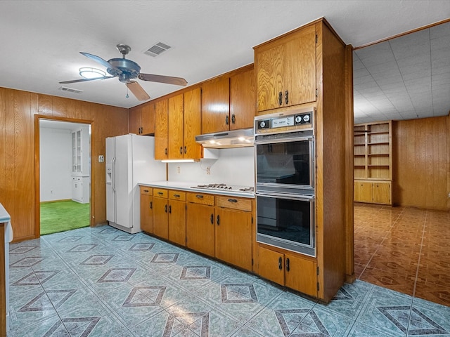 kitchen featuring double oven, under cabinet range hood, white refrigerator with ice dispenser, visible vents, and light countertops