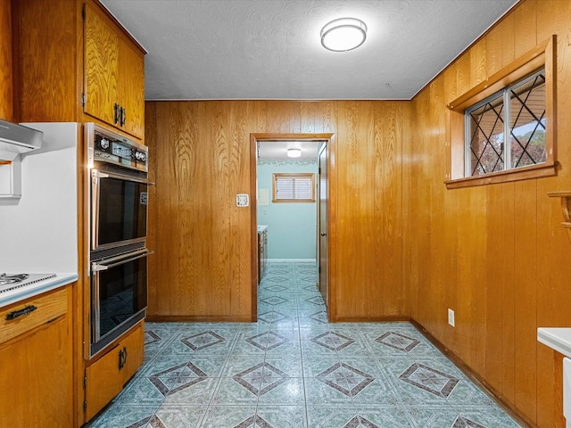 kitchen featuring light countertops, wood walls, brown cabinetry, and dobule oven black