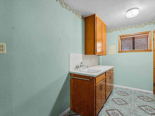 kitchen featuring light countertops, brown cabinetry, a sink, and baseboards