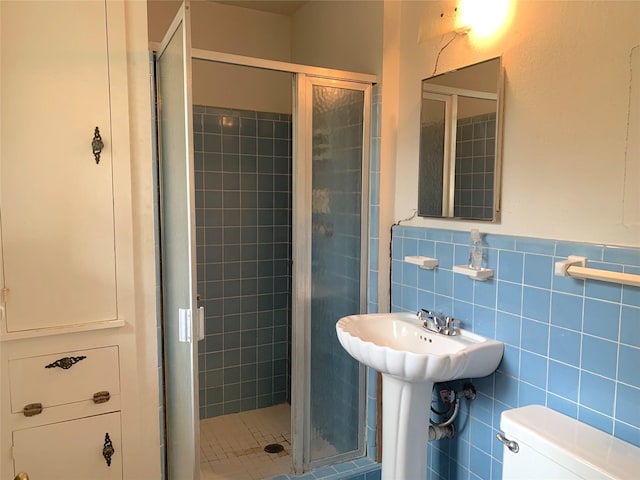 bathroom with tile walls, sink, a shower with door, and toilet