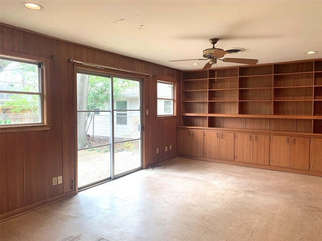 unfurnished living room featuring ceiling fan, built in features, and wood walls