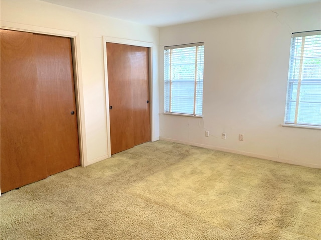 unfurnished bedroom with light carpet and two closets