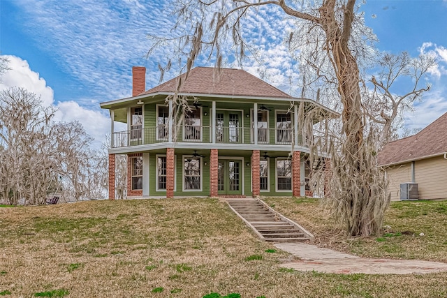 view of front of house featuring cooling unit, ceiling fan, a balcony, and a front lawn