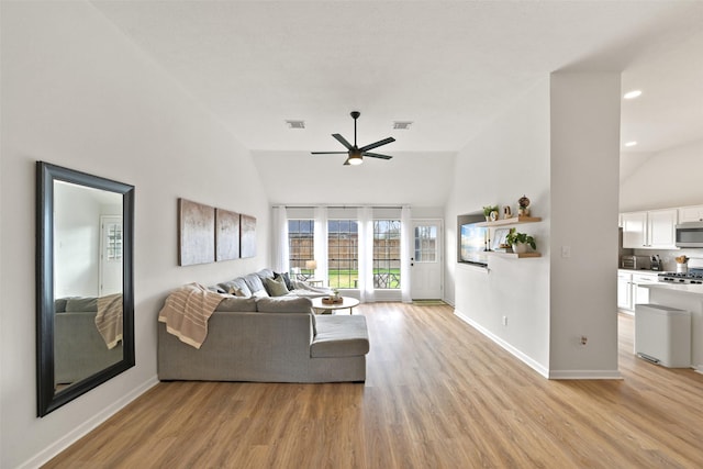 living room with visible vents, baseboards, light wood-style floors, and lofted ceiling