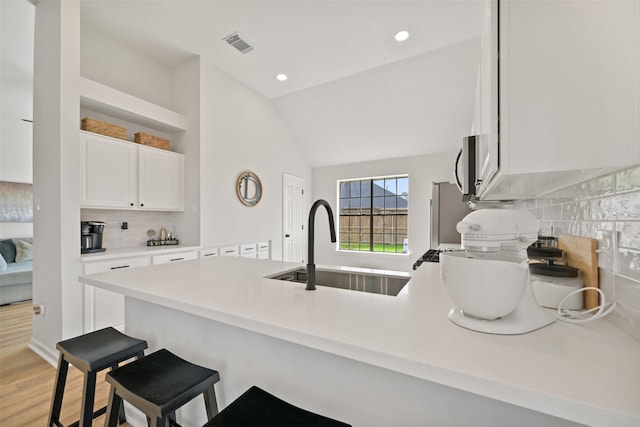 kitchen featuring visible vents, stainless steel microwave, a breakfast bar area, a peninsula, and white cabinets