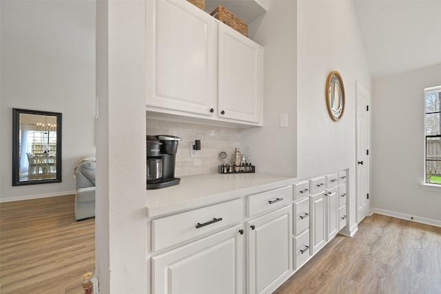 bar with tasteful backsplash, baseboards, light wood-style floors, and vaulted ceiling