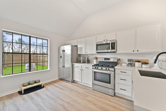 kitchen with stainless steel appliances, light countertops, lofted ceiling, and a sink