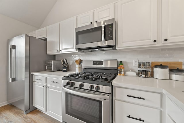 kitchen with lofted ceiling, stainless steel appliances, light countertops, white cabinets, and tasteful backsplash