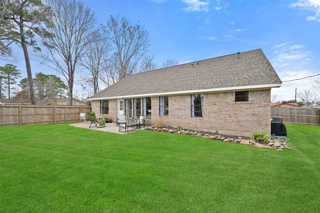 rear view of property with a patio, a yard, a fenced backyard, a shingled roof, and brick siding