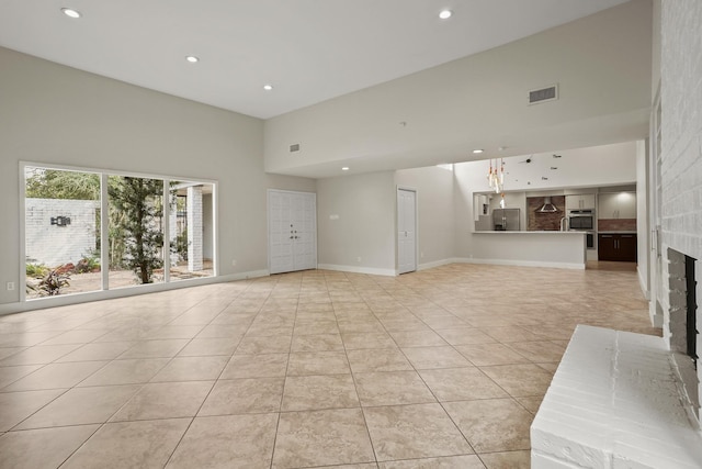 unfurnished living room featuring a high ceiling, light tile patterned flooring, and a brick fireplace